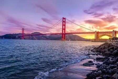 的 金门大桥 at sunset with a multicolored sky 和 the San Francisco Bay in the foreground.