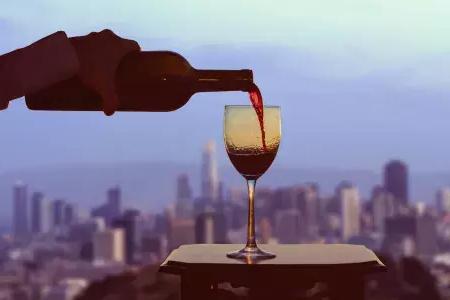 A glass of red wine being poured, with the San Francisco skyline visible out the window.