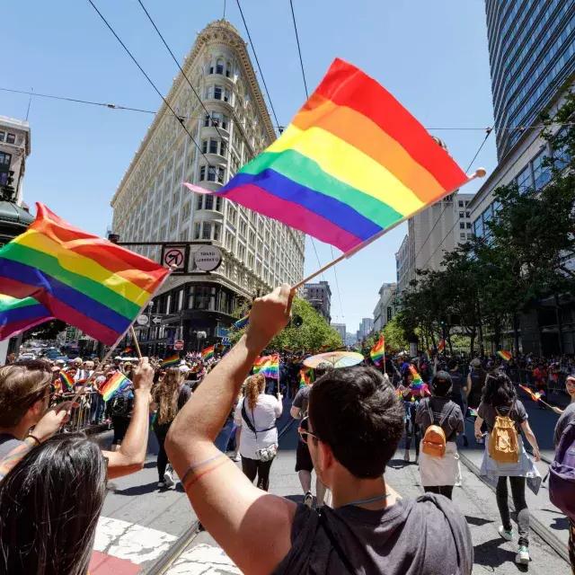 走在贝博体彩app同志游行队伍中的人们挥舞着彩虹旗.